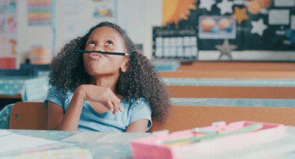 Shot of a young girl looking bored while playing at a school desk